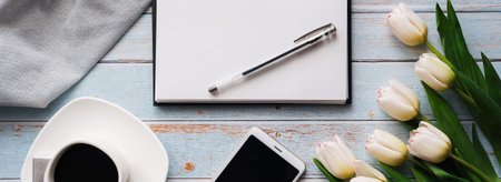 Spring blanks of a freelancers workplace with a bouquet of white tulips, a smartphone, an empty...