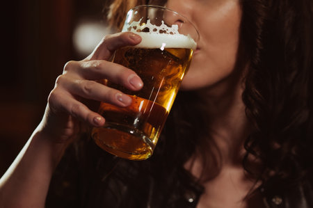 woman sexually drinks from a glass of beer lager with foamの写真素材