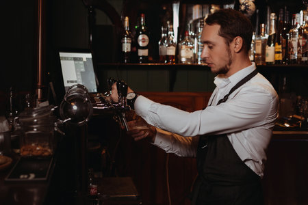 bartender at the bar pours beer into a glass with a tap