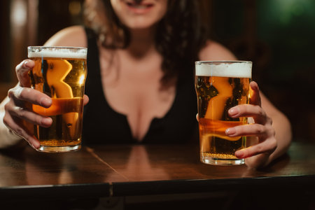 two glasses of light foam beer lager in the hands of a woman with big sexy breasts at the barの写真素材