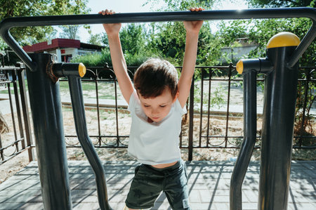 child boy playing and climbing on horizontal bars on playground in summerの写真素材