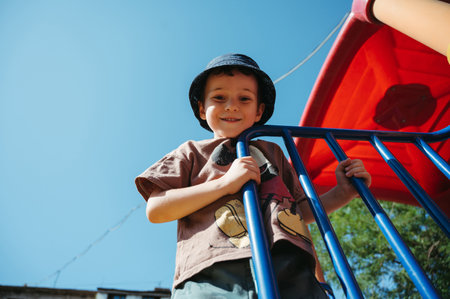 kindergarten boy plays on slide on playground in summer on the streetの写真素材