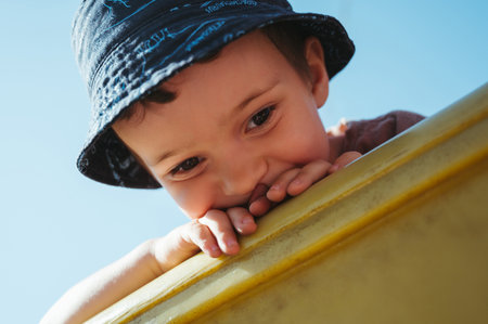 kindergarten boy plays on slide on playground in summer on the streetの写真素材