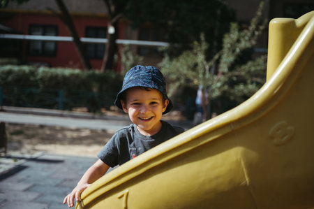 happy kindergarten boy rides a slide on playground in summerの写真素材