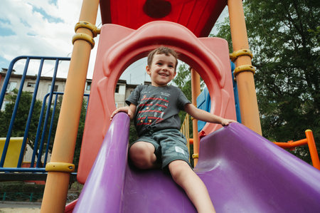 preschooler boy plays on a slide on playground in summerの写真素材