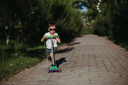 preschooler boy rides a scooter in park in summerの写真素材