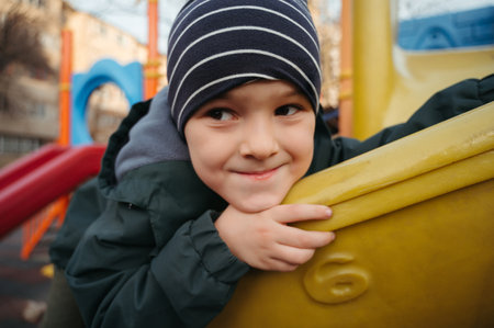 happy child boy playing on slide on playground in autumn