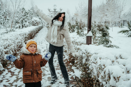 Happy funny moms with child boy son playing in park in the snow
