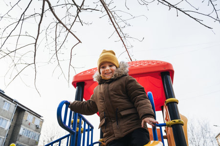 Happy child kid boy playing on a slide on playground in winter in the park