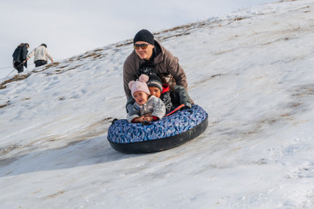 TAU SAMALY, KAZAKHSTAN - DECEMBER 23, 2023: happy Kazakhs family tubing down a slide in winter with...
