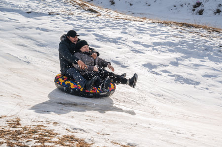 TAU SAMALY, KAZAKHSTAN - DECEMBER 23, 2023: happy Kazakhs family tubing down a slide in winter with snow at Tau Samaly recreation center in Kazakhstanのeditorial素材