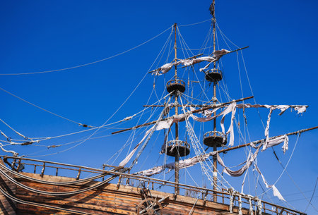 mast with sails on an ancient wooden pirate ship against background of blue sky in ocean