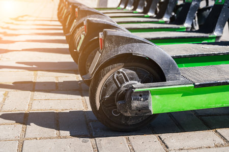 wheels of green electric scooters standing in a row for rental on sidewalk in city in summer on...