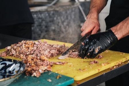 male chef cut boiled beef meat with knife on a cutting board for cooking oriental Uzbek pilaf in...