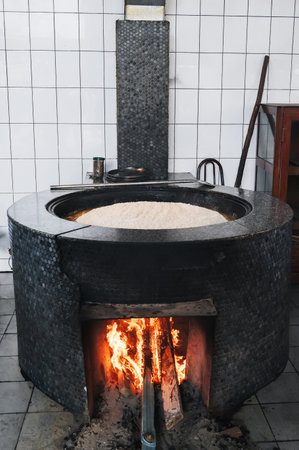 traditional Uzbek pilaf is cooked in large cauldron on a wood-burning stove with fire in kitchen of Asian oriental restaurant in Uzbekistanの写真素材
