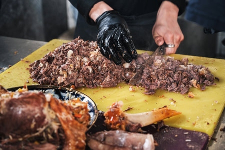 male chef cut boiled lamb meat with a knife to cook asian Uzbek pilaf in restaurant in Central Asian...