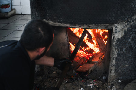 male cook lights a wood-burning stove for big cauldron for cooking Uzbek pilaf in oriental kitchen at Asian restaurant in Uzbekistanの写真素材
