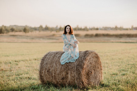 young girl sitting on haystack in field in summer. Added the effect of a small film grain