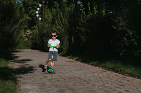 preschooler boy rides a scooter in park in summerの写真素材