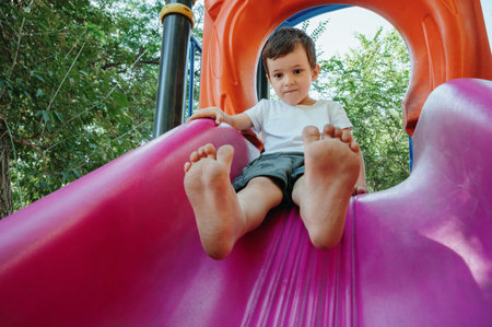 happy child kindergarten boy playing on slide on playground in summerの写真素材