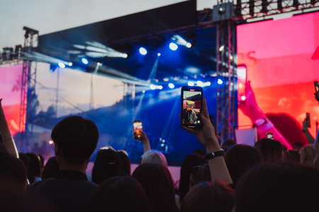 crowd of people at stage at a live music concert are shooting videos on smartphones in hands