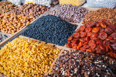 different varieties of dried fruits and nuts on counter of oriental uzbek food bazaar in Central Asia. Raisins, dried apricots, almonds, walnuts and figs in market stallの写真素材