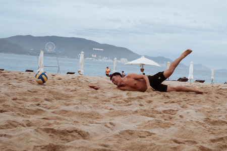 An Asian player falls while taking a ball playing beach volleyball by sea in summer in Nha Trang. Nha Trang, Vietnam - July 21, 2024のeditorial素材