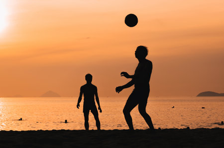 Silhouettes of men playing beach football on beach by sea at sunsetの写真素材