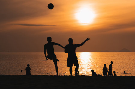 Silhouettes of a group of Asian men playing traditional beach football on beach by the sea at sunsetの写真素材