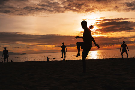 Silhouettes of Asian men ball players playing traditional beach soccer sepak takraw by sea in summer at sunriseの写真素材