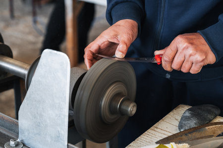 male sharpener sharpens a knife blade on knife sharpening machine in workshopの写真素材