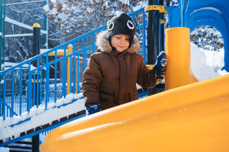 happy child boy is playing on a playground on a slide outside in winterの写真素材