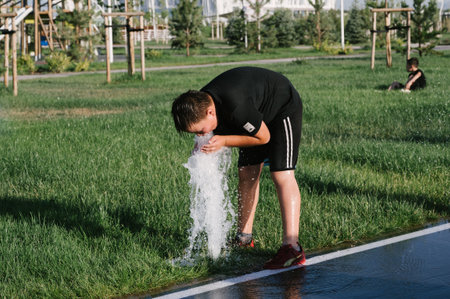 Young Asian boy drinks water from a fountain. Shymkent, Kazakhstan - July 4, 2024のeditorial素材