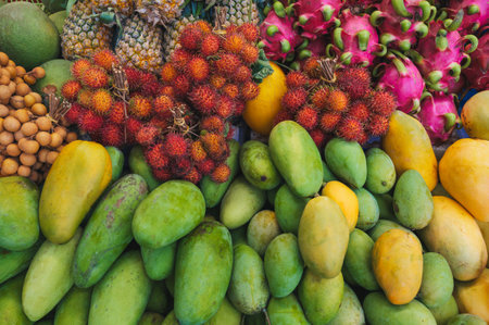 assortment of various tropical exotic Asian fruits on counter in a store in Vietnam. Vietnamese yellow and green mangoes, dragon fruit and rambutanの写真素材