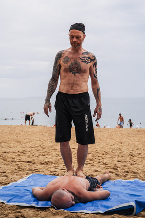 Man does a foot massage standing on back of lying man on beach by sea in summer on vacation. Nha Trang, Vietnam - July 25, 2024のeditorial素材