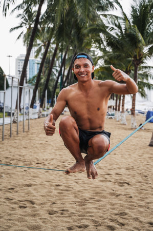 A happy young male acrobat smiles while sitting on slackline on the beach in summer. Nha Trang, Vietnam - July 29, 2024のeditorial素材