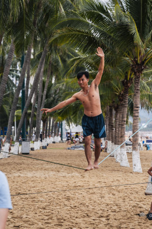 Asian acrobat man walks on tightrope between palm trees on the beach for slackline training. Nha Trang, Vietnam - July 25, 2024のeditorial素材