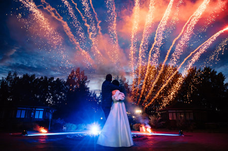 bride and groom stand with their backs against the background of festive fireworks on wedding dayの写真素材