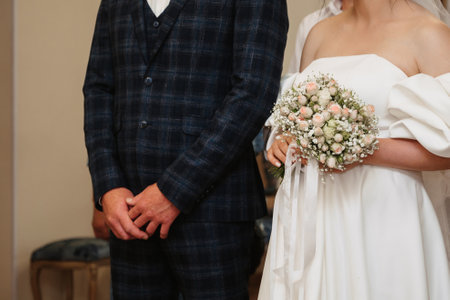 hands of bride and groom with a bouquet in ceremonial hall on the wedding dayの写真素材