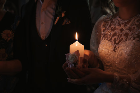 hands of the bride and groom hold a lighted candle on the wedding dayの写真素材