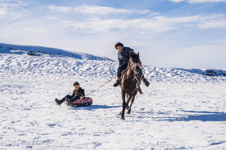 Kazakh boys ride horses and tubing in winter in steppe in Kazakhstan. Shymkent, Kazakhstan - January 27, 2024のeditorial素材