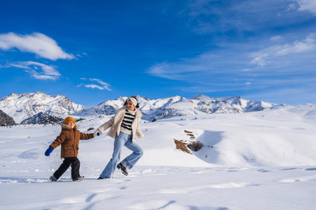 Mom and son running on a snow-covered slope against the backdrop of a mountain landscape in winterの写真素材