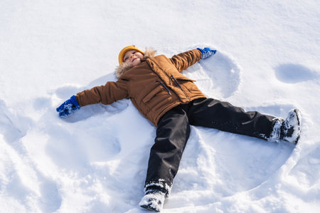 A boy lies in the snow and makes a snow angelの写真素材