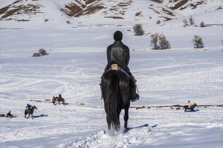 The back of a Kazakh teenager on a horse in steppes of Kazakhstan in winter. Shymkent, Kazakhstan -...