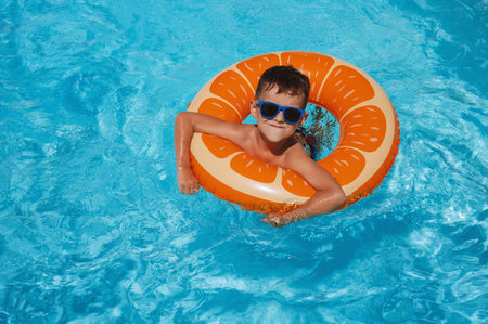 happy small child boy in inflatable circle learns to swim in the swimming pool at hotel on summer vacationの写真素材