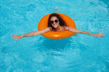 happy young girl in sunglasses rests in an inflatable circle in pool at a hotel on vacation in summer holidaysの写真素材