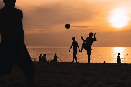 Silhouettes of a group of Asian men playing traditional beach football on beach by the sea at sunsetの写真素材