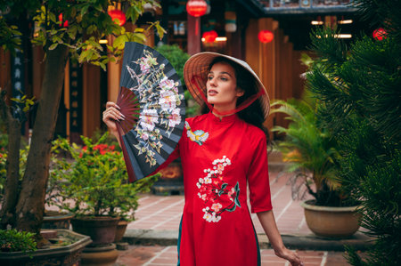 happy young female tourist traveler in a Vietnamese hat with a fan at the temple on pagoda in Hoi An in Asia in Vietnamの写真素材