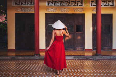 back of a beautiful woman traveler in a dress and a traditional Vietnamese hat at pagoda in Vietnam...