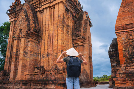 back of Asian male tourist traveler in a Vietnamese cone hat Non La on the Cham Towers of Po Nagar in Nha Trang in Vietnam in Asiaの写真素材